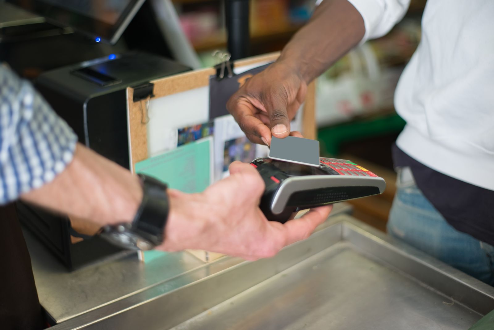 A customer tapping a bank card on a payment terminal at a checkout