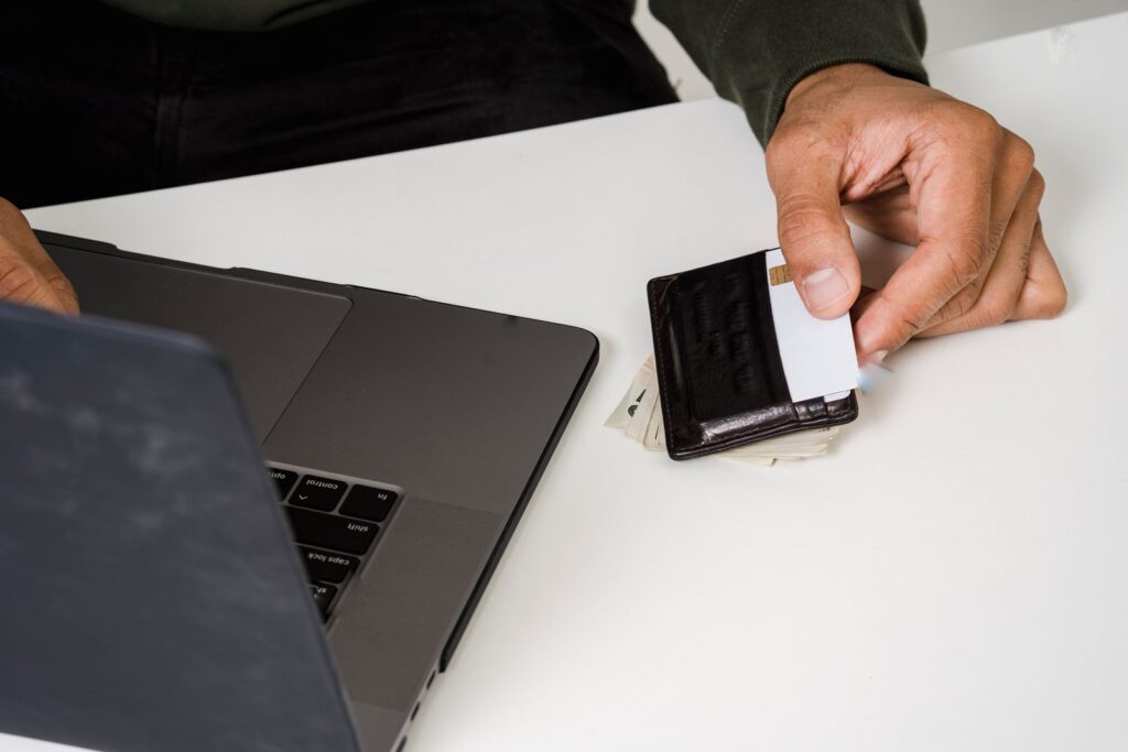 A hand holding a credit card from a wallet beside a laptop